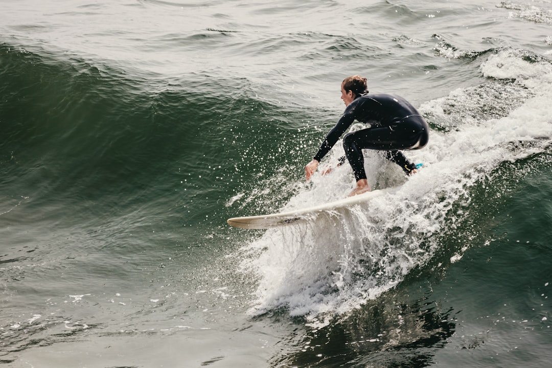 Glued to the Wave by Surf Brands man in black wet suit riding white surfboard on green sea during daytime