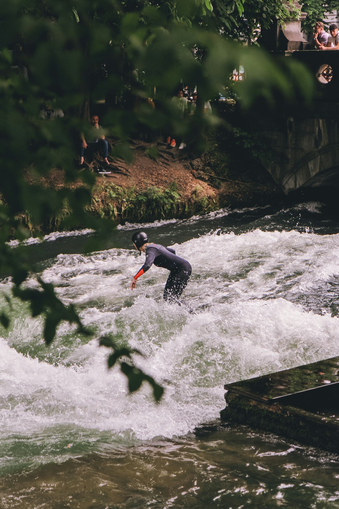 A surfer enjoying the unique experience of river surfing in the middle of the city of Munich 🌊 by Surf Brands a man riding a surfboard on top of a river